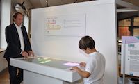 Ein Mann und ein Bub stehen sich spielend an einem Tisch gegenüber
