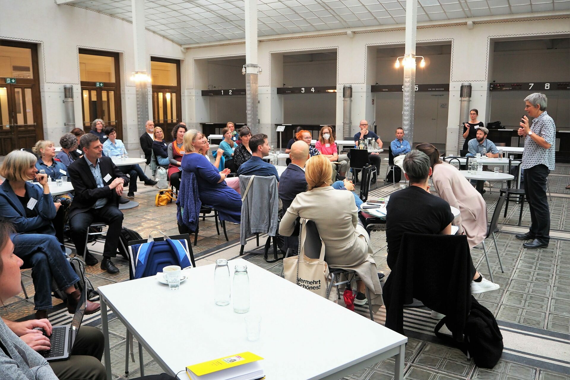 Menschen in großem Raum, sitzen an Tischen und diskutieren miteinander