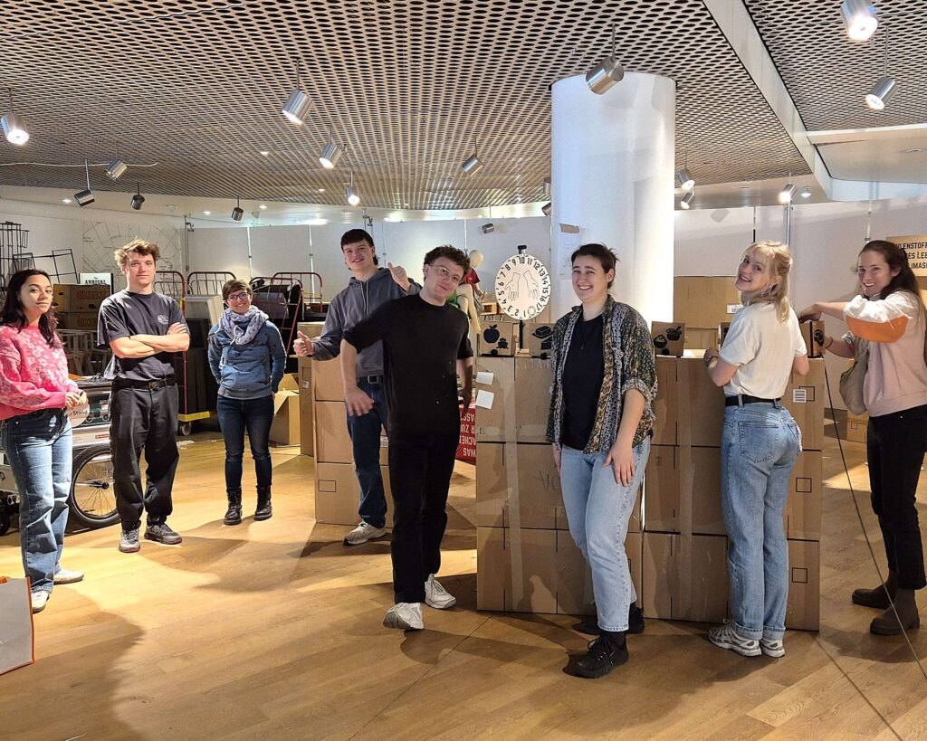 Mehrere Personen stehen nebeneinander zwischen Kartons